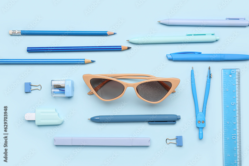 Stylish sunglasses with stationery supplies on blue background