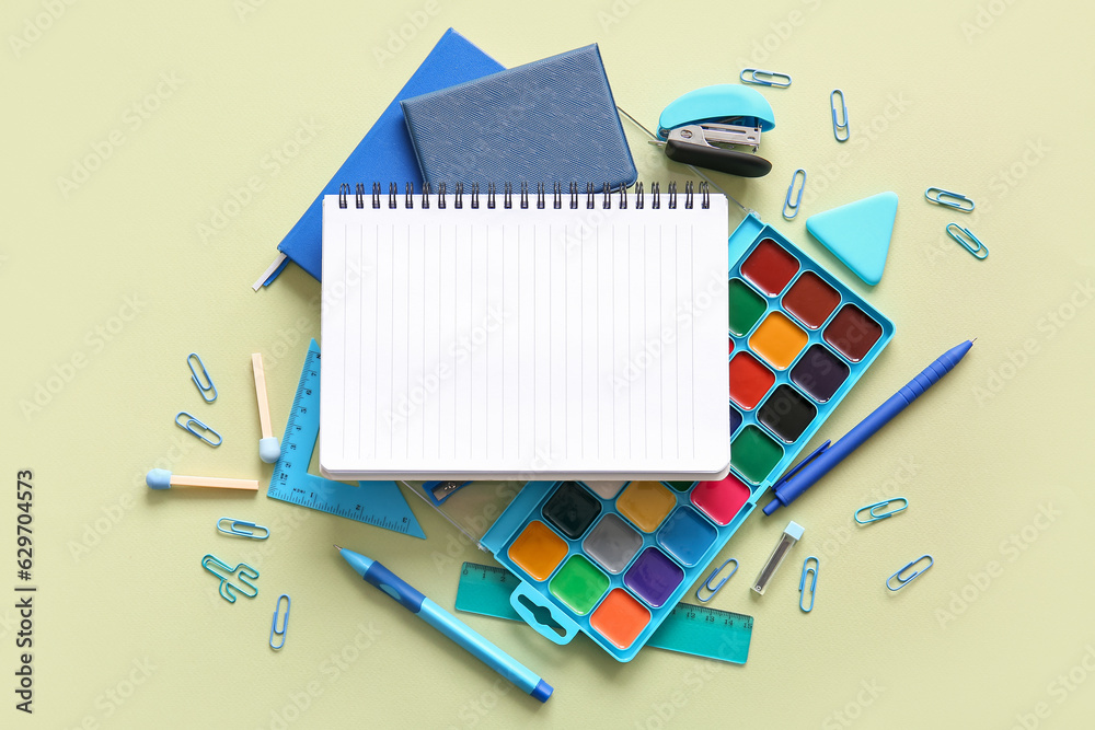 Composition with blank notebook and different school stationery on green background