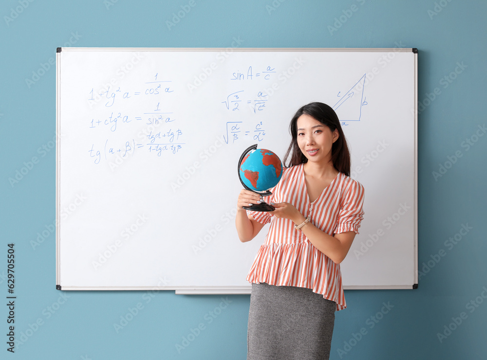 Female Asian teacher with globe near flipboard in classroom