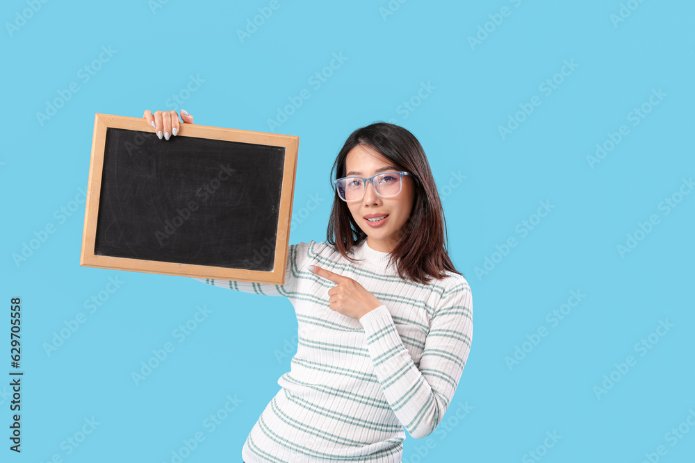 Female Asian teacher pointing at chalkboard on blue background