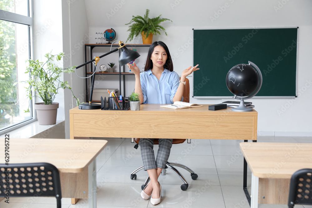 Female Asian teacher sitting at table in classroom