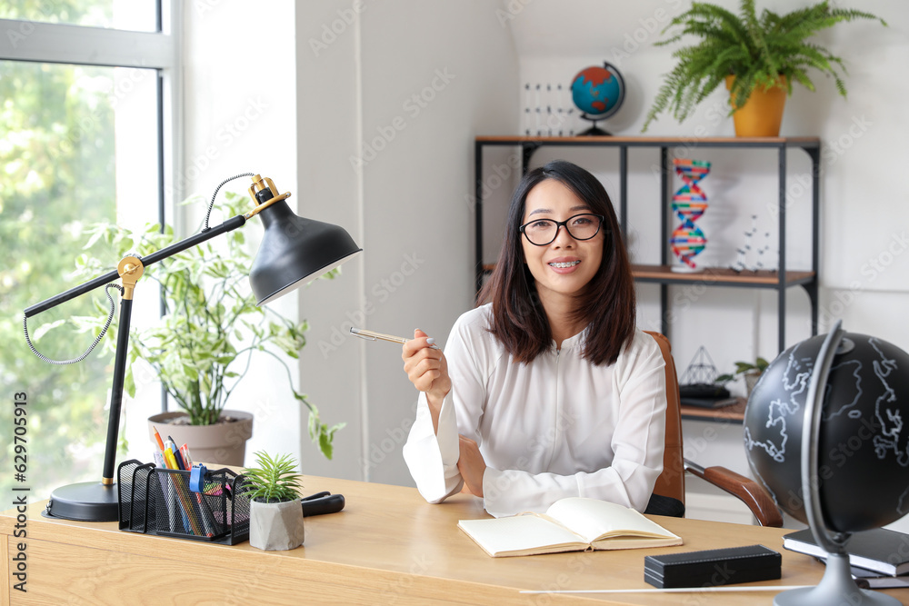 Female Asian teacher sitting at table in classroom