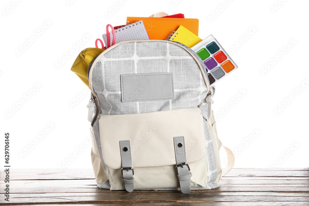 Grey school backpack with notebooks, watercolors and scissors on wooden table near white background