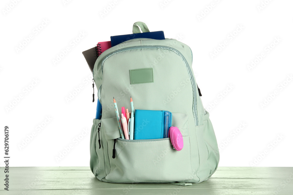 Green school backpack with notebooks, pencils and pens on wooden table near white background