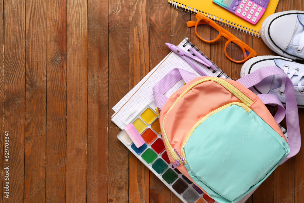 Colorful school backpack with eyeglasses, sneakers and different stationery on wooden background