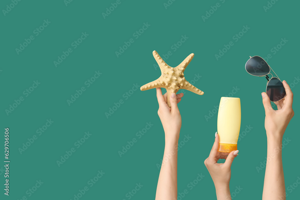 Female hands with bottle of sunscreen cream, sunglasses and starfish on green background