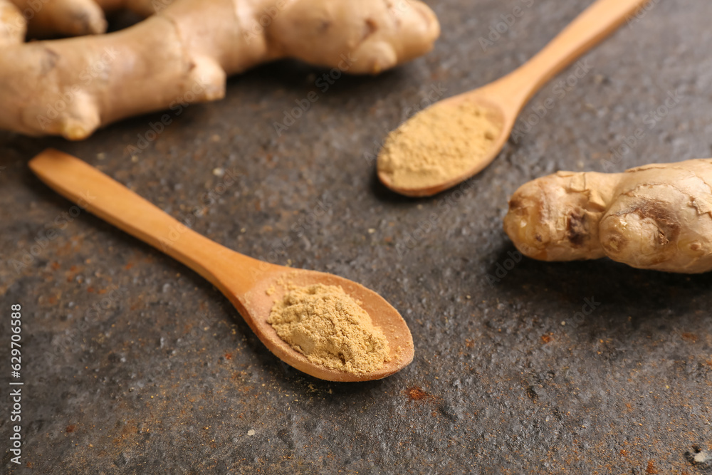 Fresh ginger roots and wooden spoons with dried powder on dark background