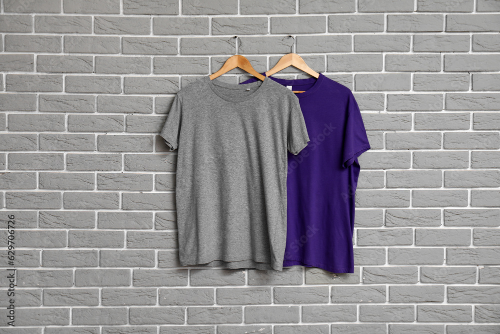 Stylish t-shirts hanging on grey brick wall