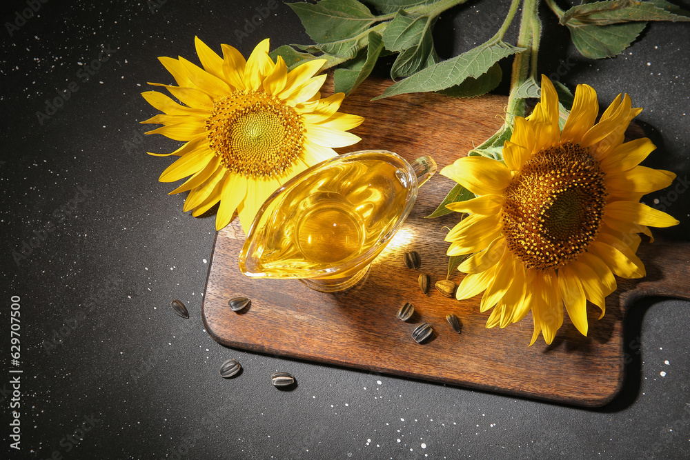 Wooden board with gravy boat of sunflower oil and seeds on black background