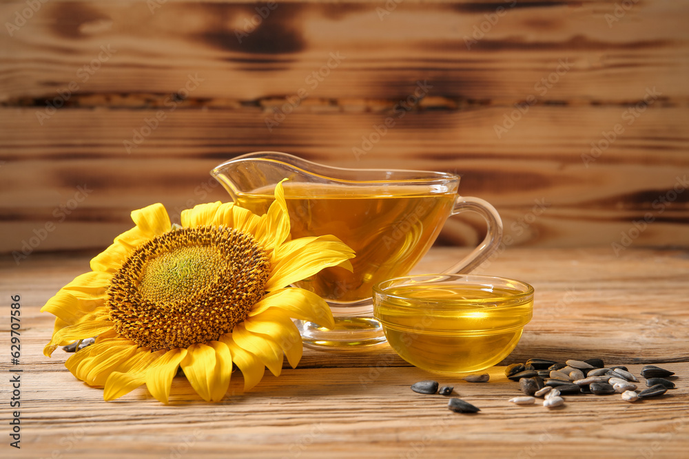 Gravy boat and glass bowl of sunflower oil with seeds on wooden background