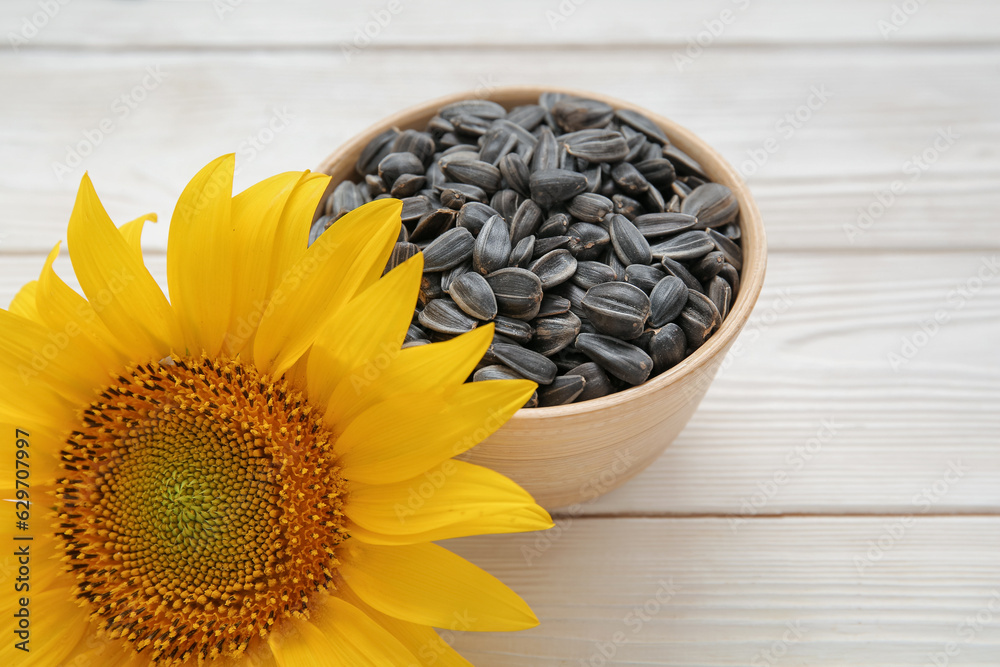 Beautiful sunflower and bowl with seeds on white wooden background