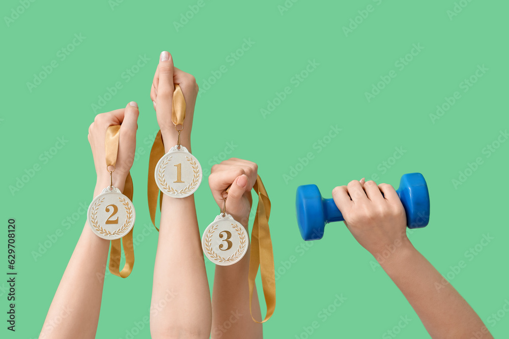 Female hands with dumbbell and medals on green background