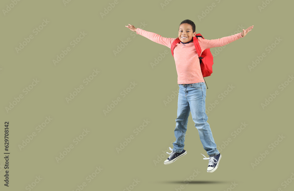 Jumping African-American boy with school backpack on green background