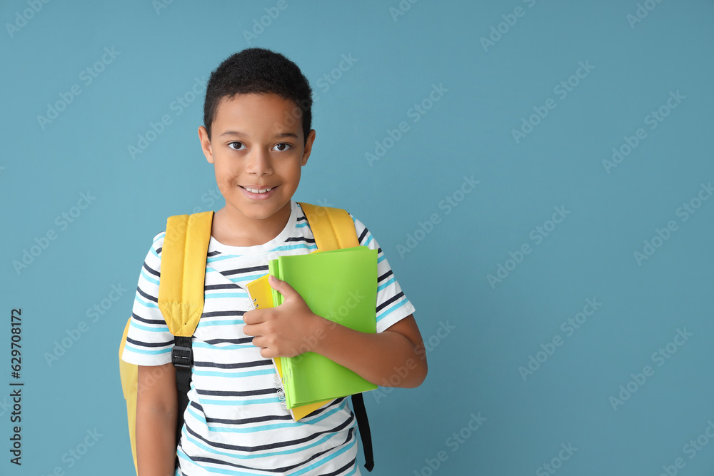 Little African-American boy with school backpack and copybooks on blue background