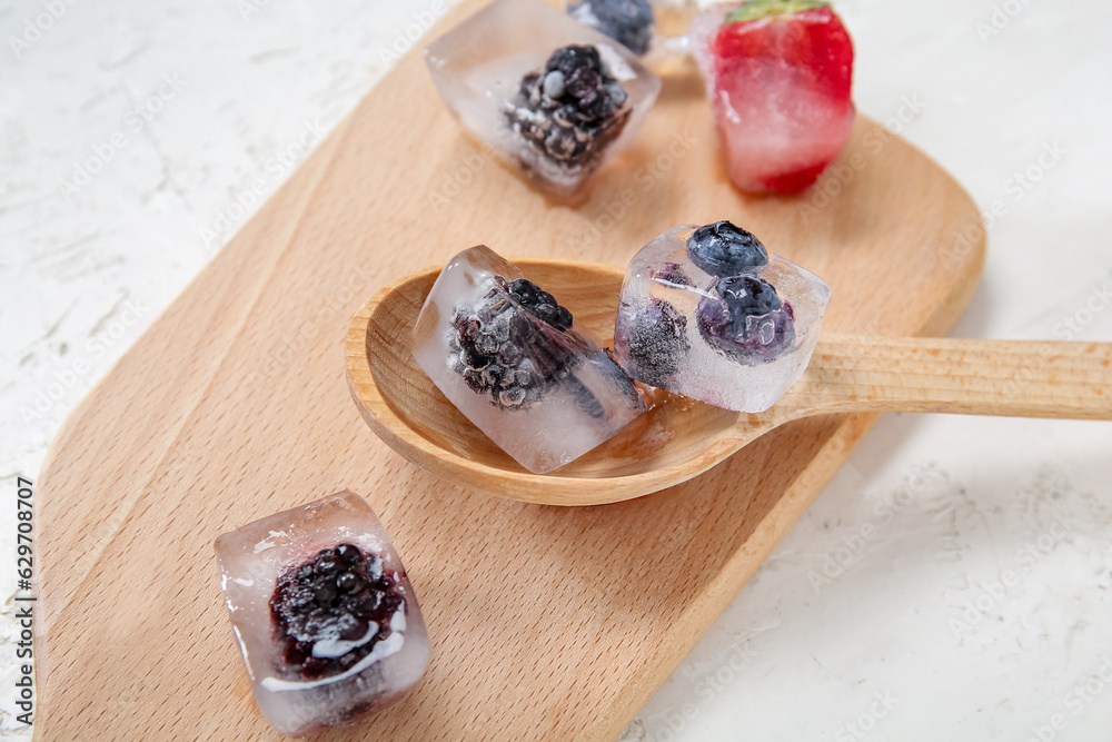 Wooden board with frozen berries in ice cubes on white background