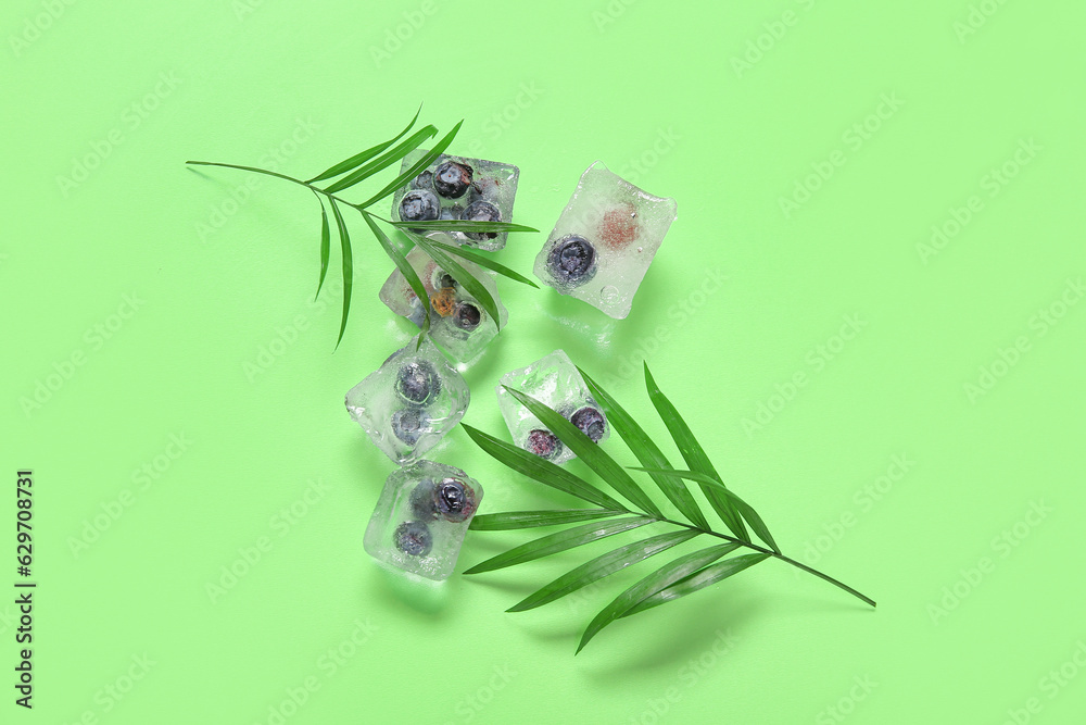 Frozen blueberries in ice cubes and palm leaves on green background