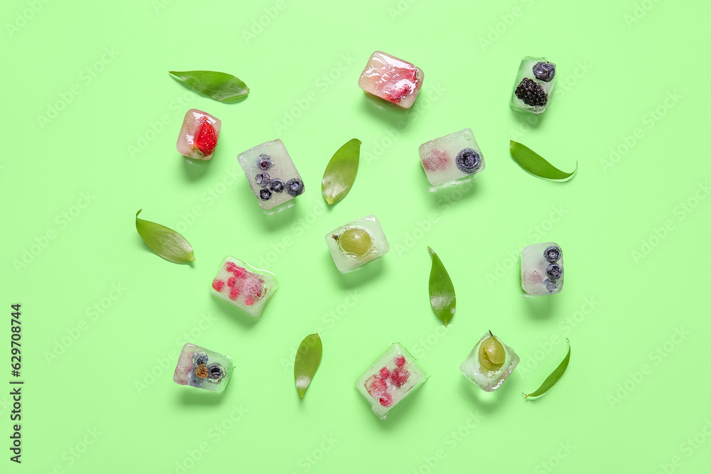 Frozen berries in ice cubes and leaves on green background