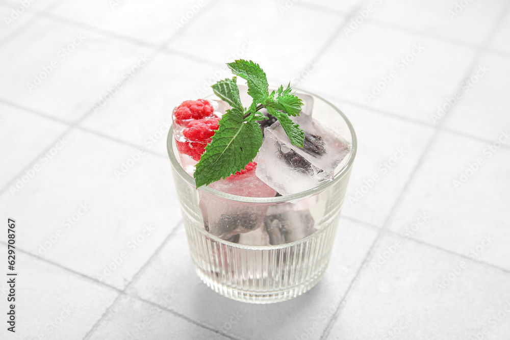 Glass with frozen berries in ice cubes and mint on white tile background