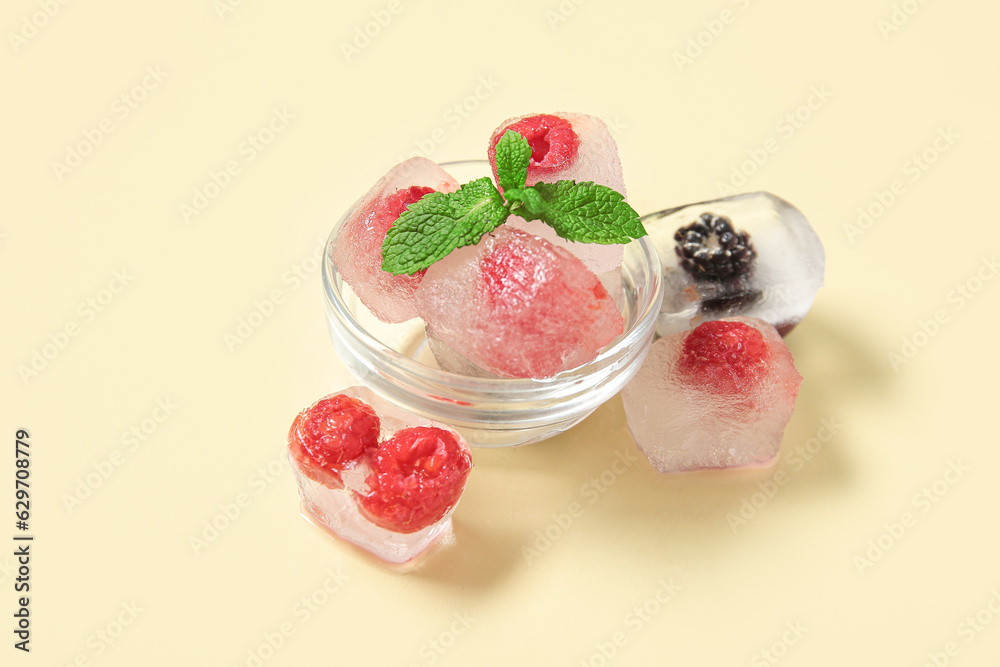 Glass bowl with frozen berries in ice cubes and mint on yellow background