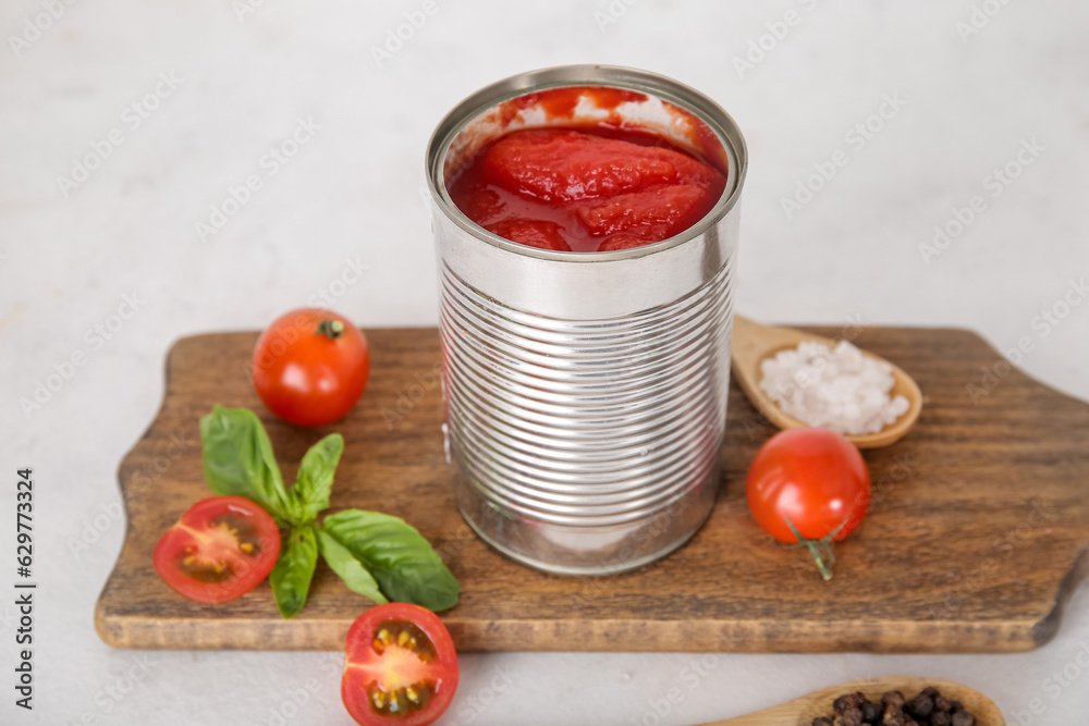 Wooden board with canned tomatoes on light background