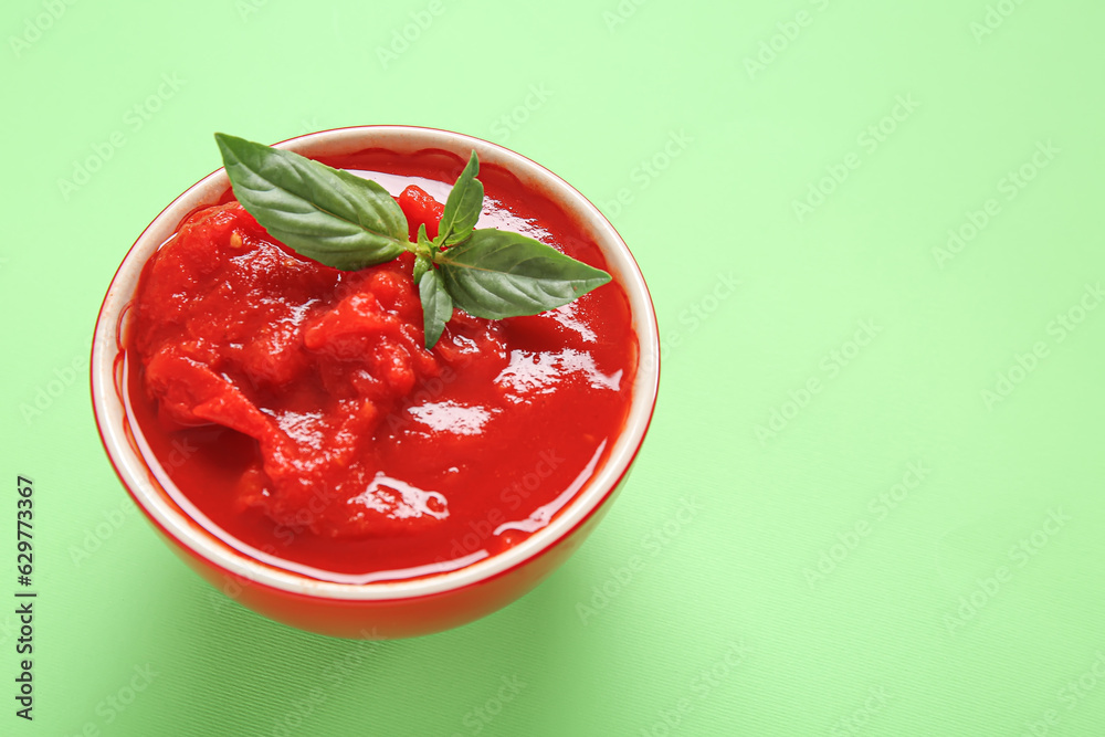 Bowl with canned tomatoes on green background