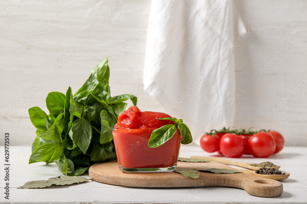 Bowl of tasty canned tomatoes, spices and basil on light wooden table