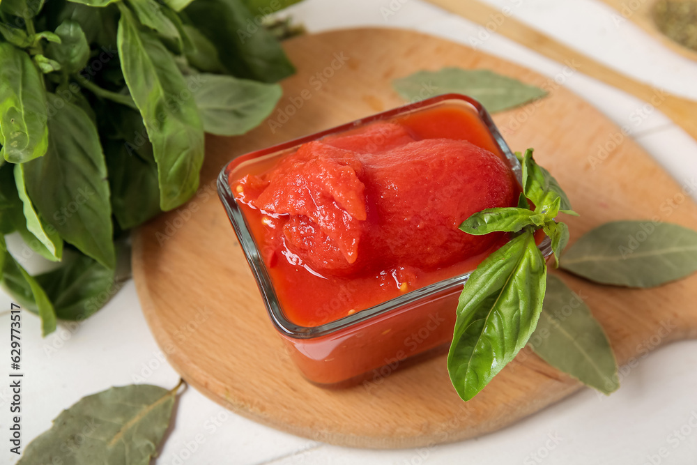 Bowl of canned tomatoes and fresh basil on light wooden table, closeup