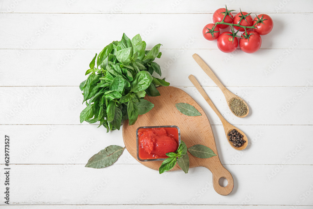 Composition with basil, spices, canned and fresh tomatoes on light wooden background