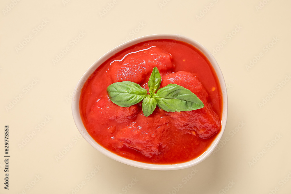 Bowl of tasty canned tomatoes with basil on color background