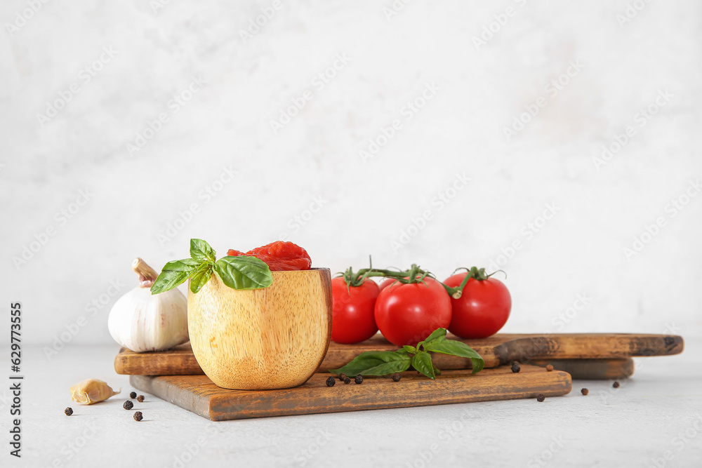 Wooden board with bowl of fresh, canned tomatoes and spices on light background