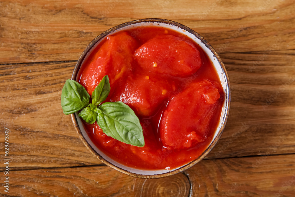 Bowl of tasty canned tomatoes on wooden background