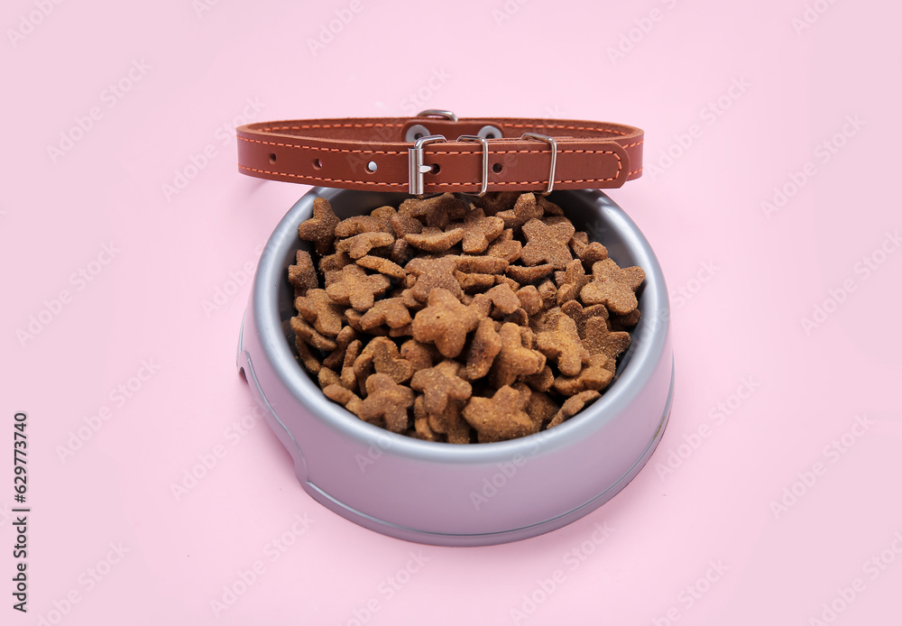 Bowl of dry pet food and collar on pink background