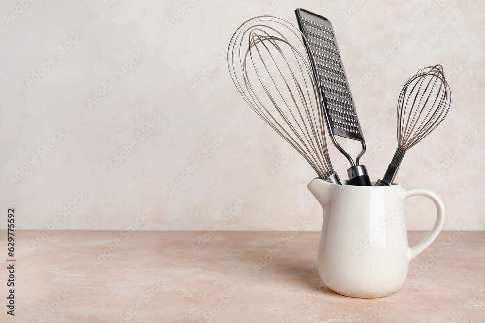 Ceramic pitcher with kitchen utensils on table against light background