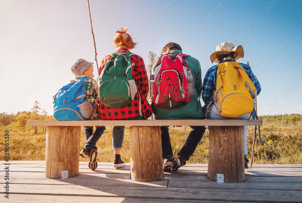 Mother and father with two sons sitting and relaxing on the bench after hiking.