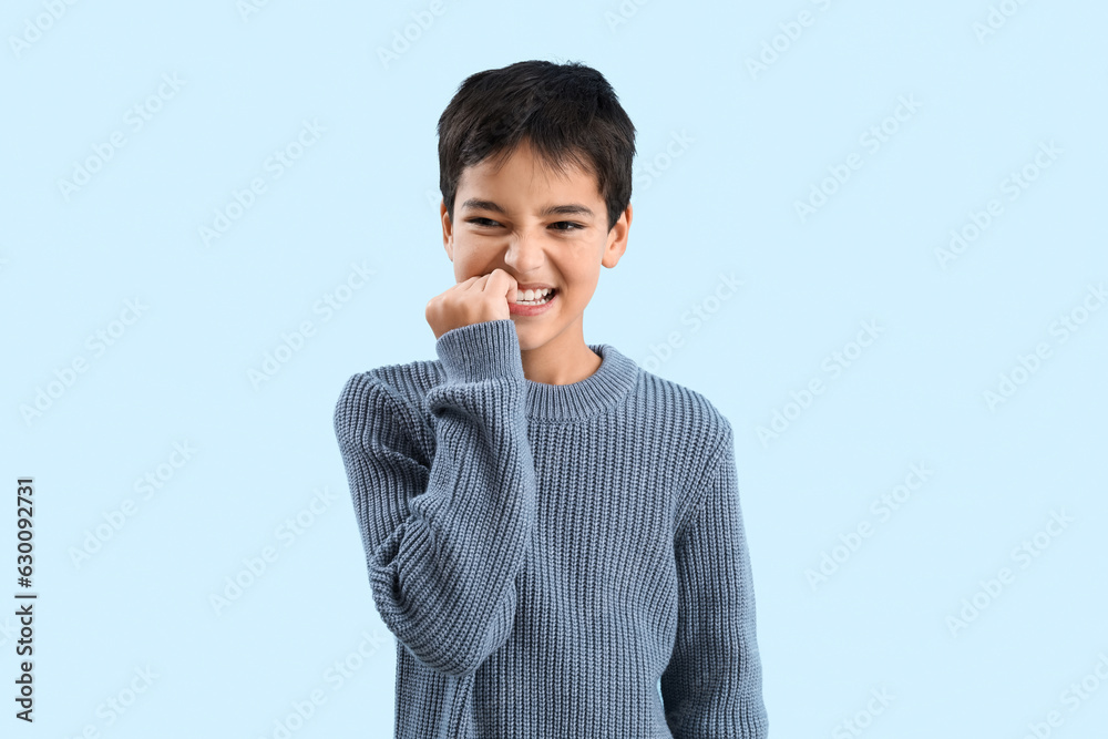 Angry little boy biting nails on blue background