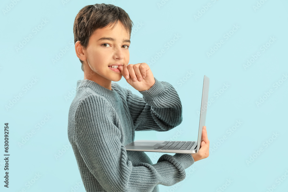 Little boy with laptop biting nails on blue background