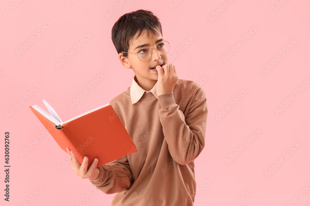 Little boy with book biting nails on pink background