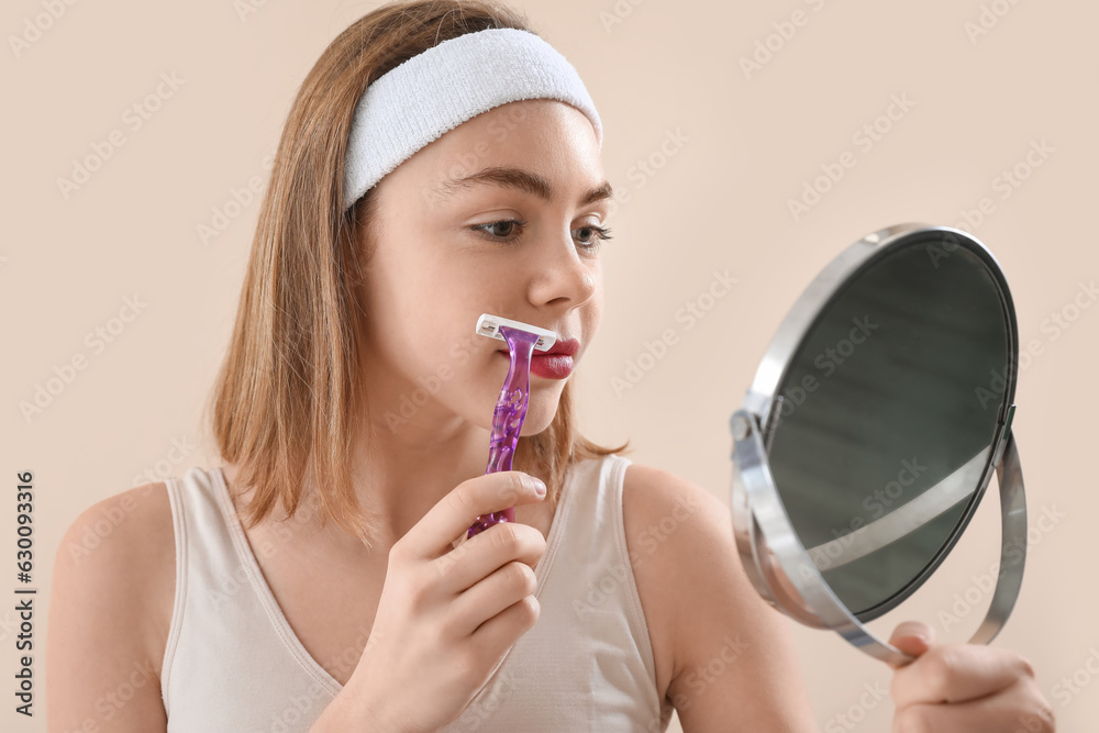 Young woman with mirror shaving face on beige background, closeup