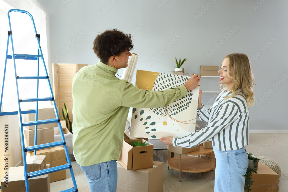 Young couple wrapping painting with stretch film in bedroom on moving day