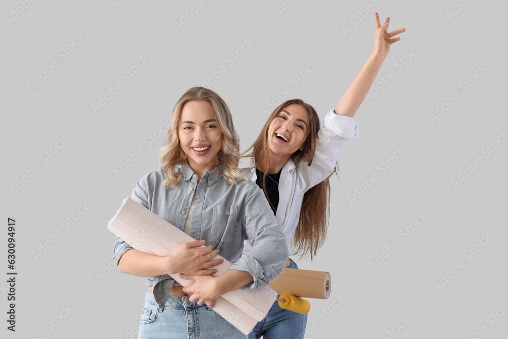 Young women with wallpaper rolls on grey background