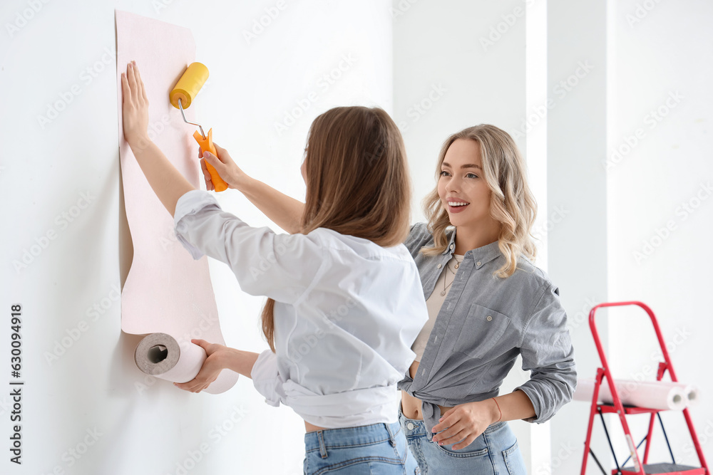 Young women gluing wallpaper at home