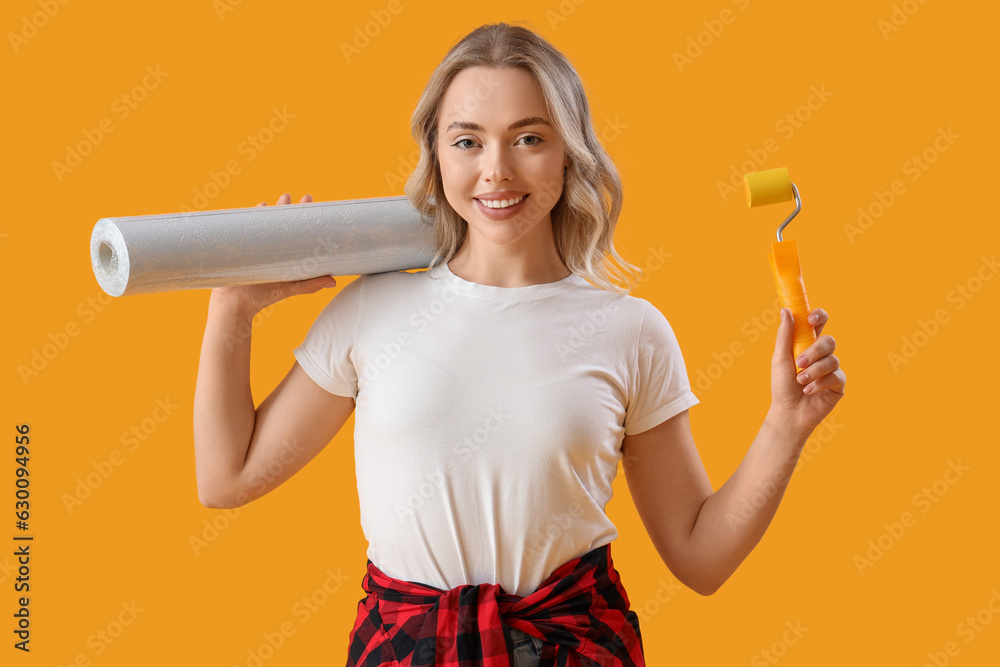 Young woman with wallpaper and roller on yellow background