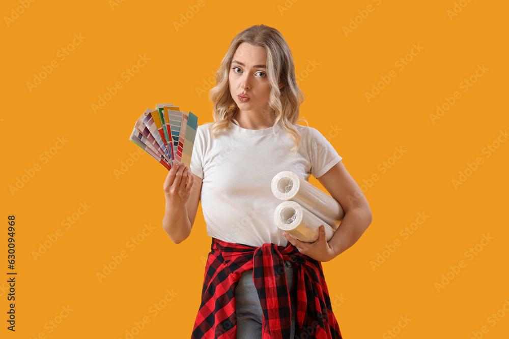 Thoughtful young woman with wallpaper rolls and color palettes on yellow background