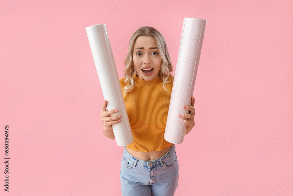 Worrying young woman with wallpaper rolls on pink background