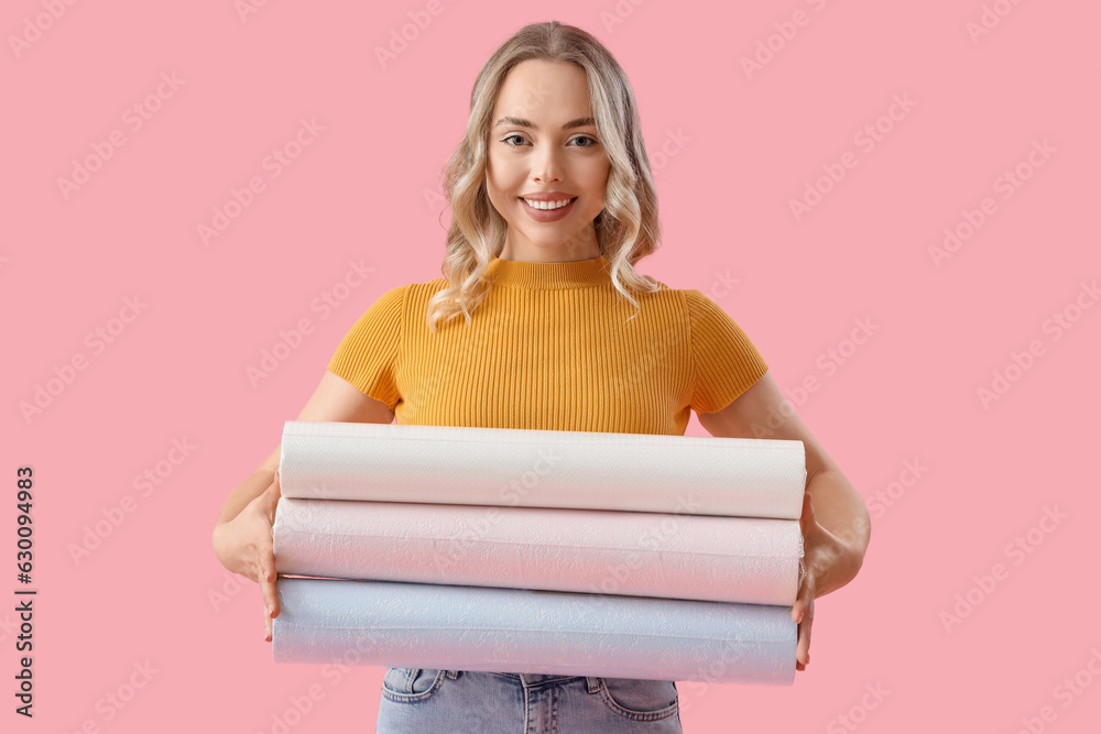 Young woman with wallpaper rolls on pink background