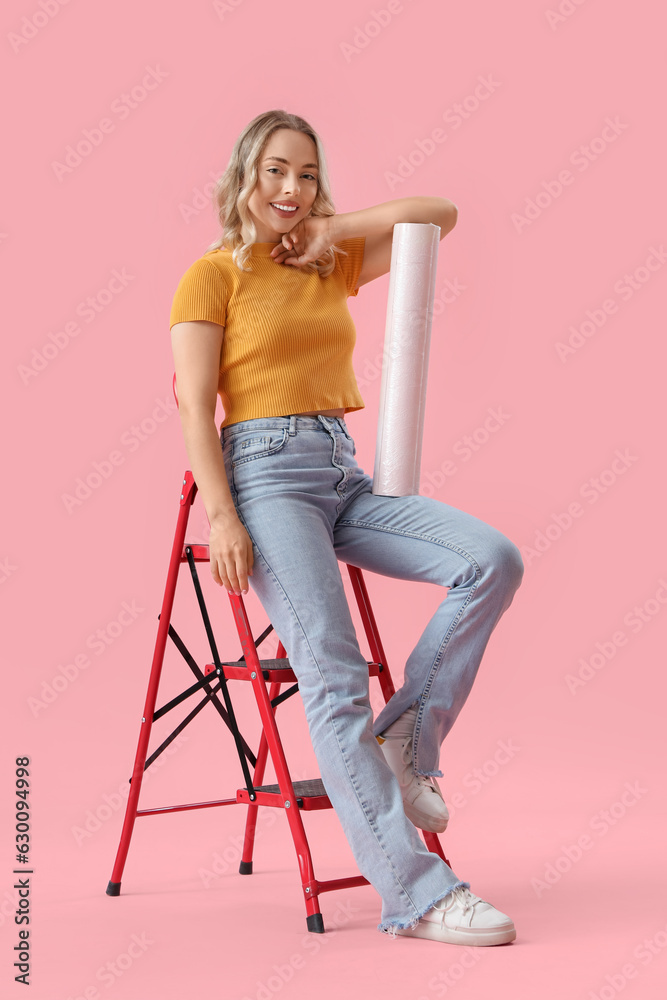 Young woman with wallpaper roll and ladder on pink background