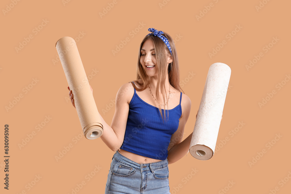 Young woman with wallpaper rolls on beige background