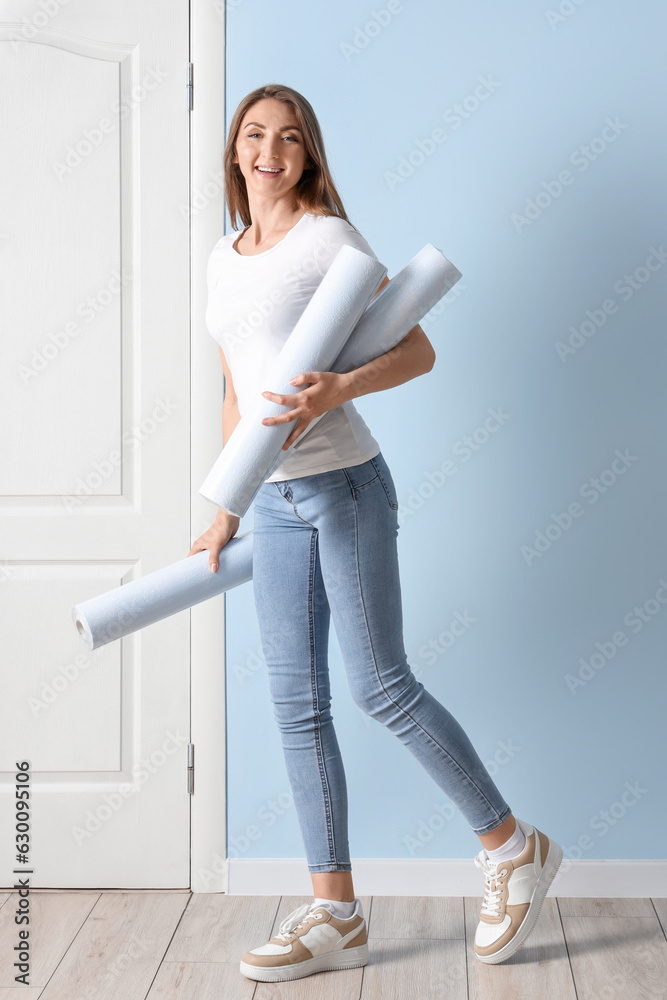 Young woman with wallpaper rolls near blue wall