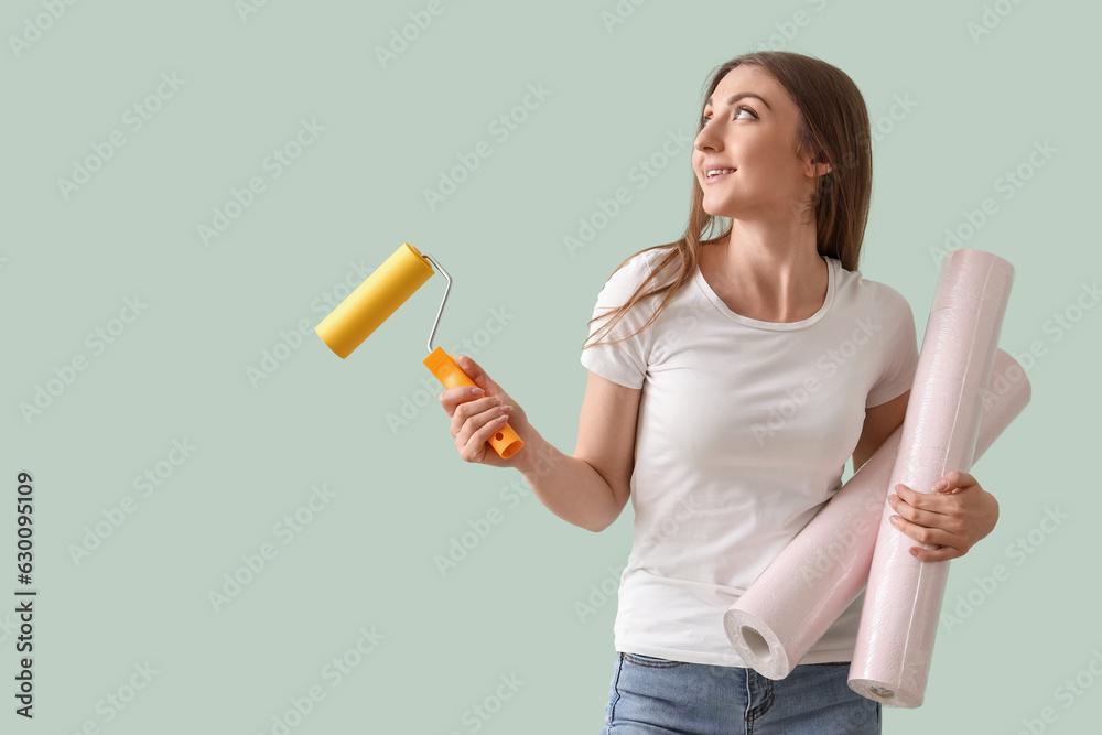 Young woman with wallpapers and roller on green background