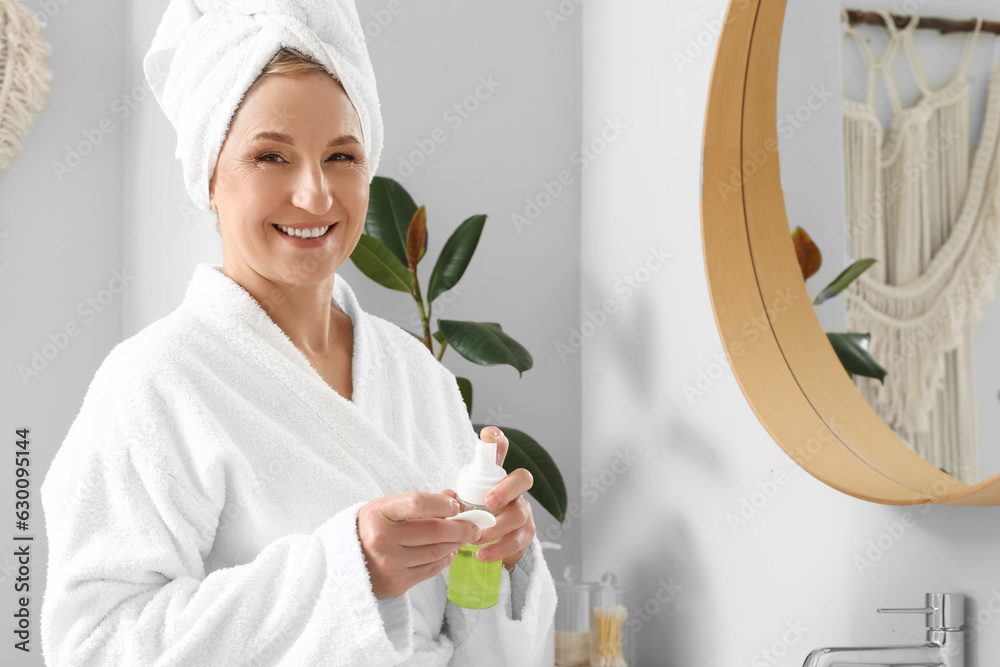 Mature woman applying cosmetic product in bathroom